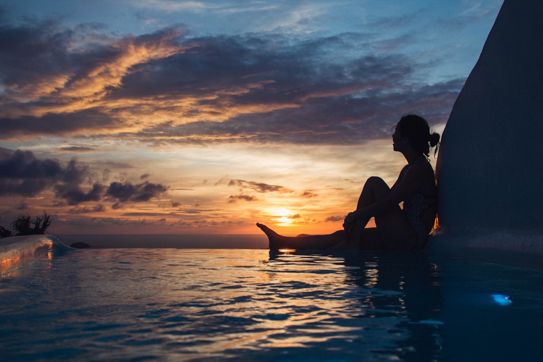 A person sits peacefully by a pool at sunset, embodying tranquility and protection, aligning with themes of shielding against negativity.