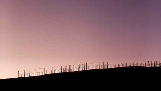 Silhouetted wind turbines on a hill against a pink sky, symbolizing energy protection and harmony, aligning with the protection charm theme.