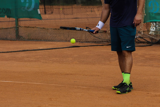 A tennis player on a clay court bouncing a ball with a racket, symbolizing focus and a shield from negativity in physical activity.